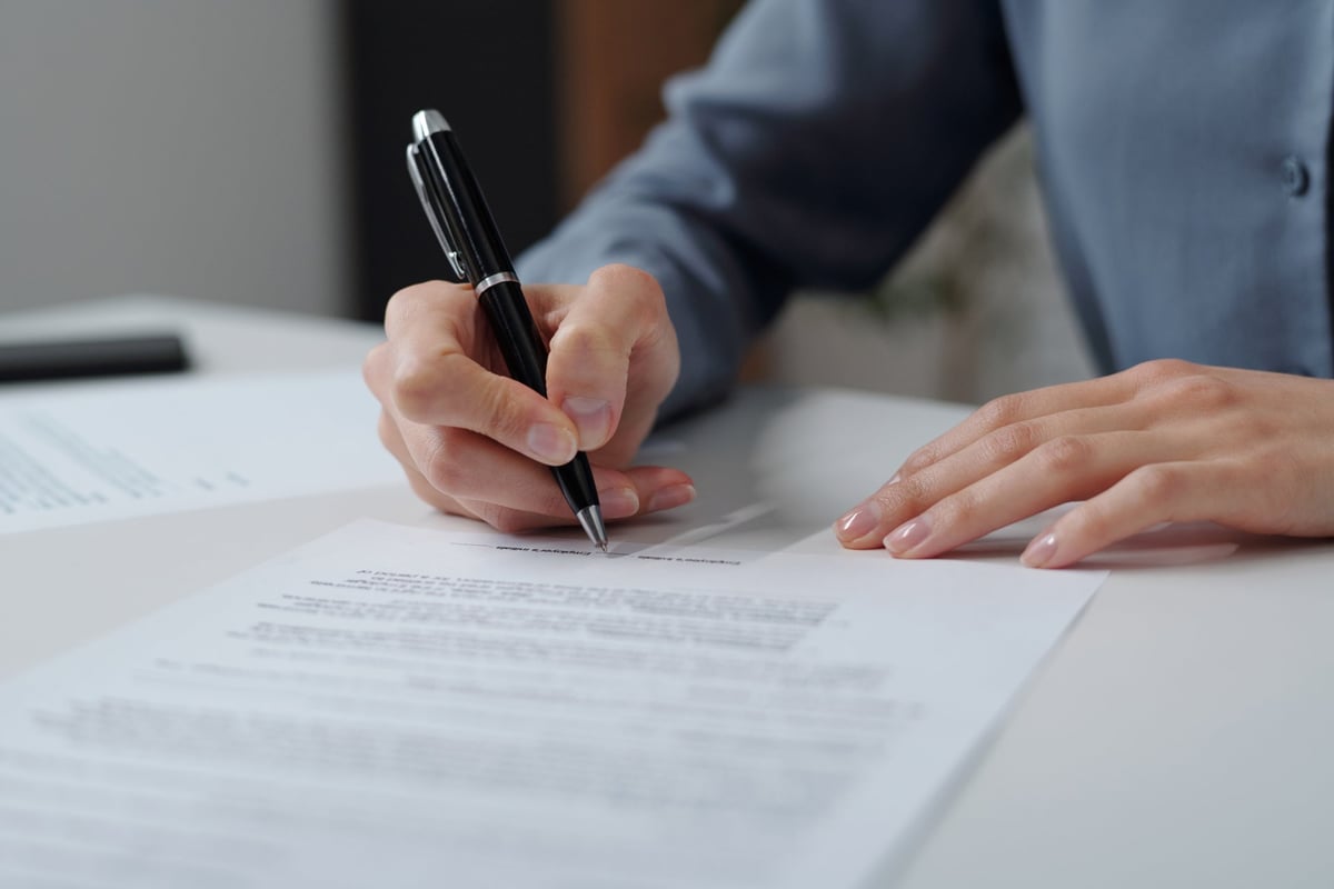 Closeup of unrecognizable businesswoman signing contract in office with focus on female hand holding pen