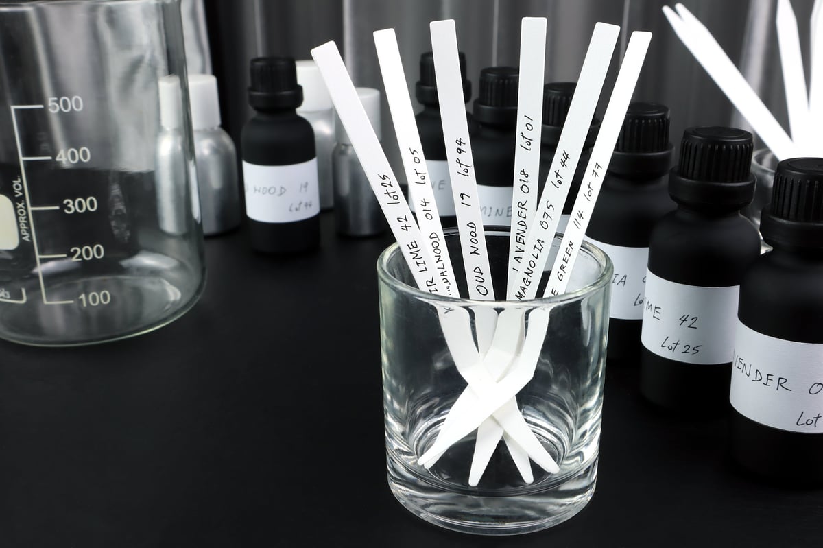 Blotter papers and fragrance oil bottles used in scent testing during perfume blending process in a laboratory setting