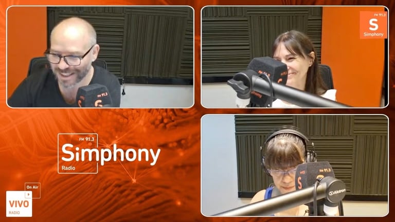Tres conductores de podcast en el estudio de grabación durante una emisión de radio, sobre fondo naranja, con micrófonos